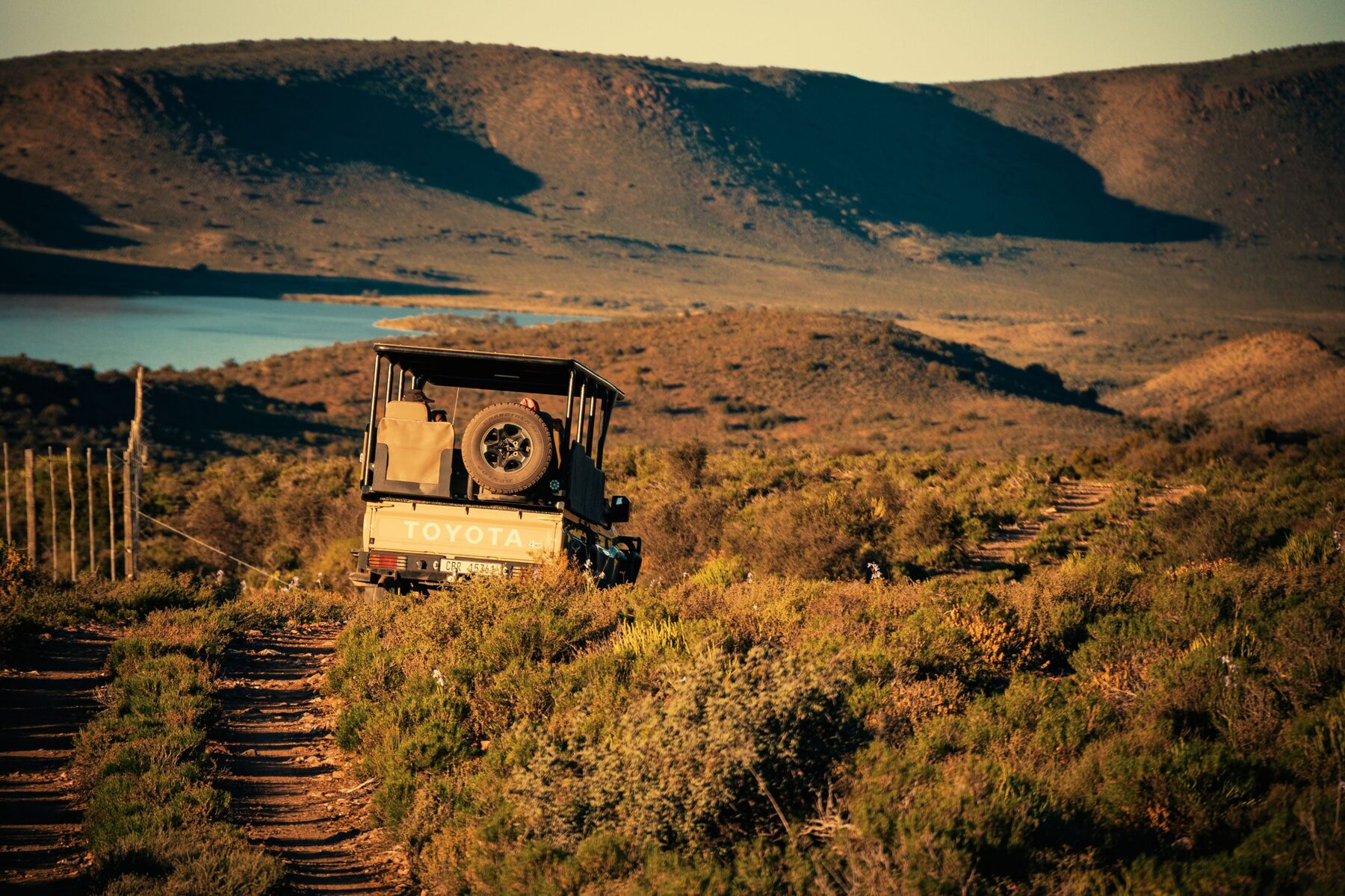 Open game-viewing vehicle on a track above a dam at sunset, South Africa