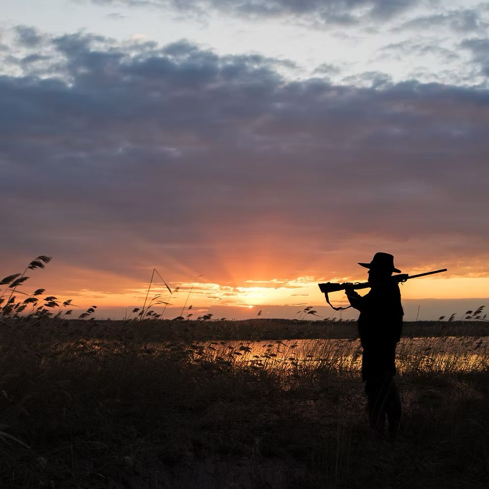 Hunter silhouetted against the sunset, rifle over his shoulder, at the end of a day in Zimbabwe