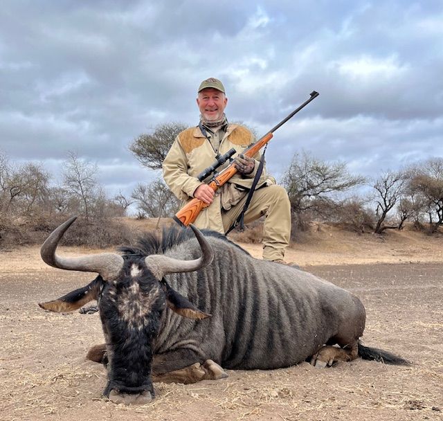 Hunter kneeling with his rifle beside a blue wildebeest bull taken in Limpopo, South Africa