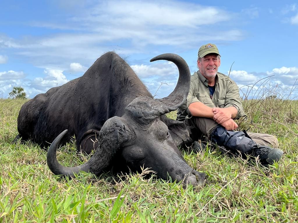 Hunting client seated beside a Cape buffalo bull in green grass, Zambezi Delta, Mozambique