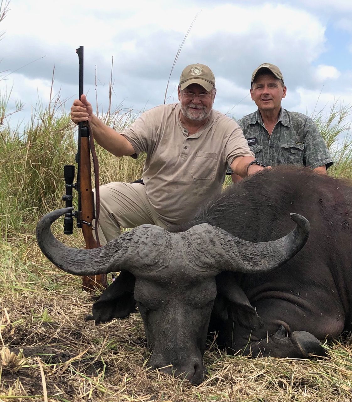 Hunting client and professional hunter with a Cape buffalo bull in Delta grass, Mozambique