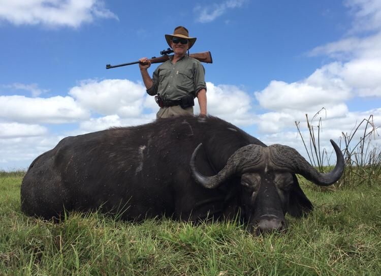 Hunter standing over a Cape buffalo bull on the Zambezi Delta floodplain, Mozambique