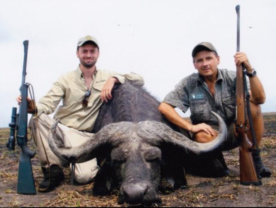 Two hunters with rifles behind a Cape buffalo bull taken in Zimbabwe