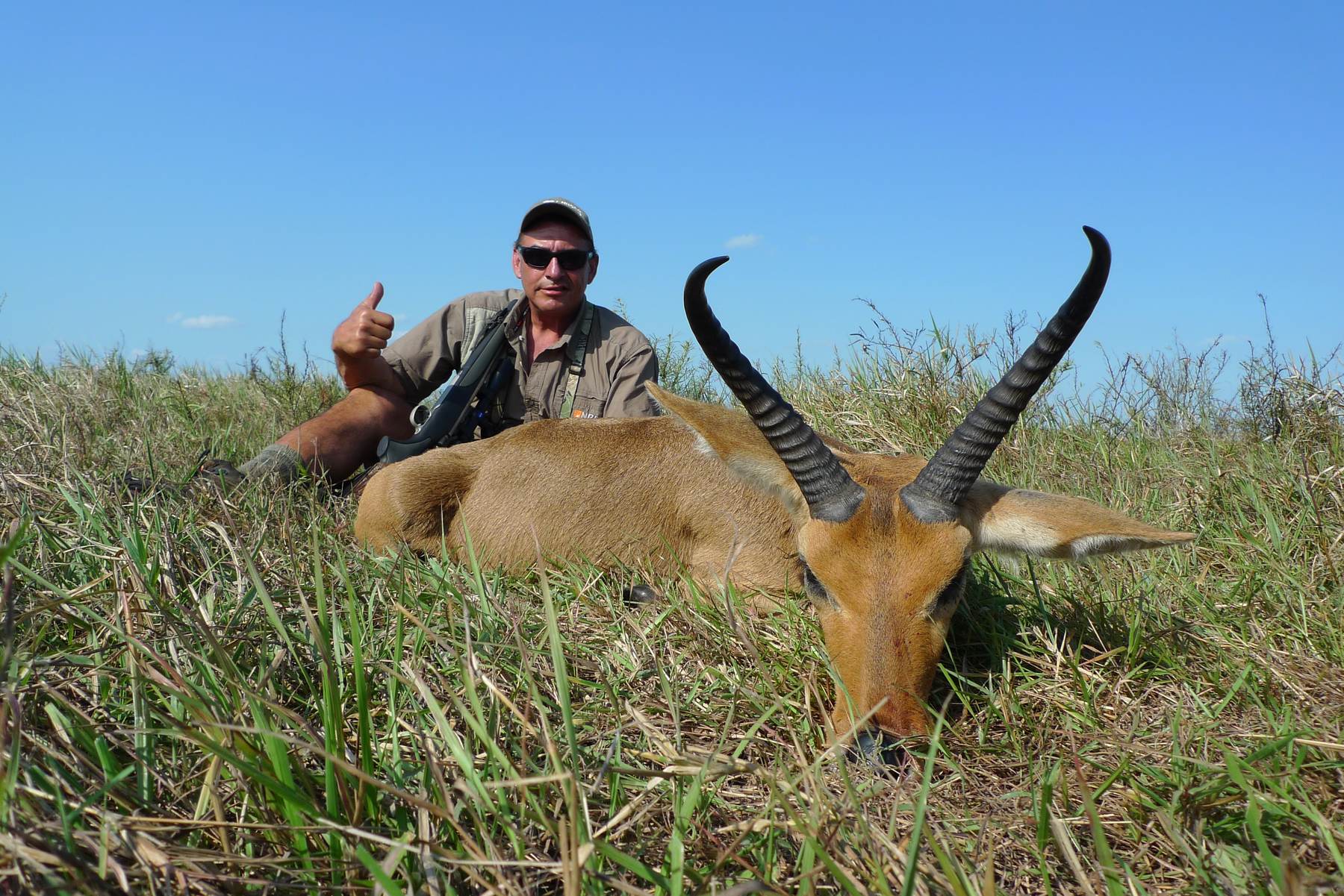 Hunting client with a reedbuck ram taken in green grass, South Africa