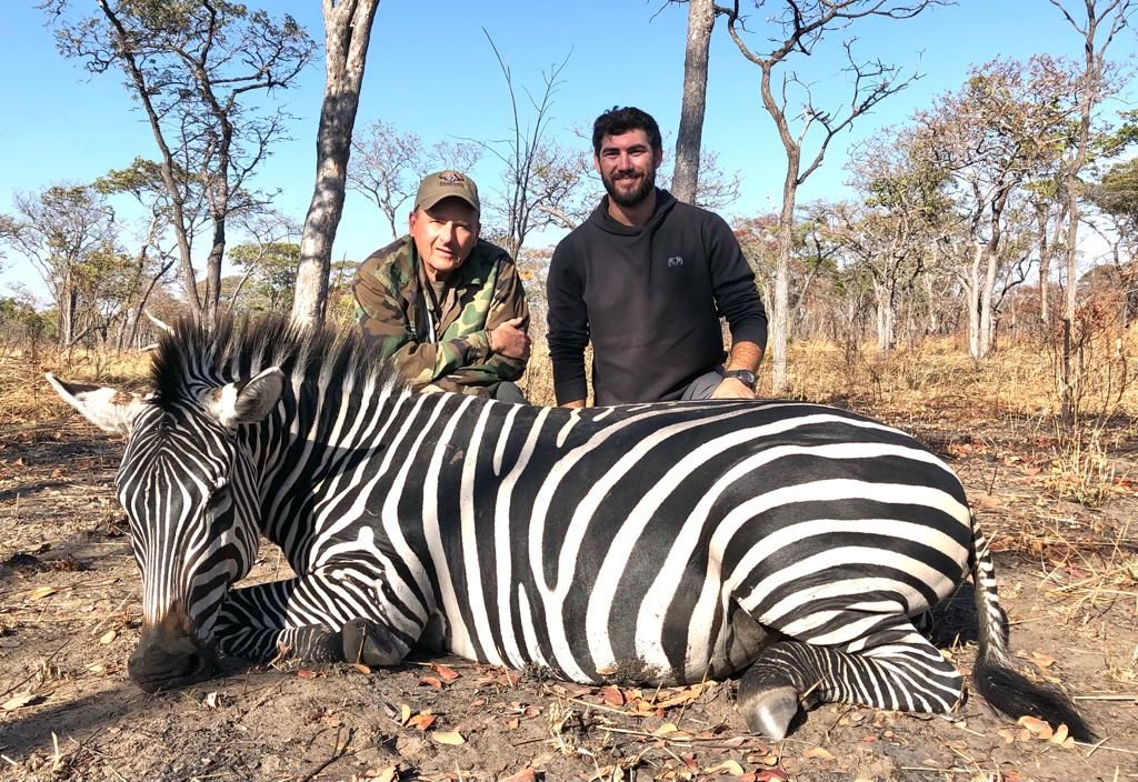 Two hunting clients with a Burchell's zebra taken in woodland, Zimbabwe